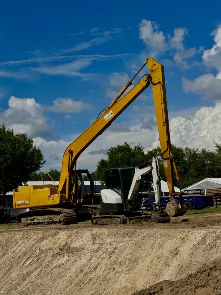 Mini excavator staged among palm trees on a land clearing site